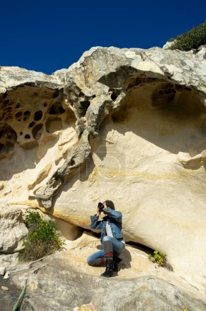 Foto de Una mujer profesional se dedica a una actividad aventurera en medio del impresionante paisaje de montaña. Ella captura la belleza de las formaciones rocosas verticales mientras toma fotos tranquilamente. - Imagen libre de derechos