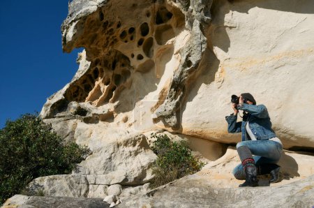 Téléchargez les photos : Un photographe se tient devant une impressionnante formation rocheuse, capturant le paysage captivant. - en image libre de droit