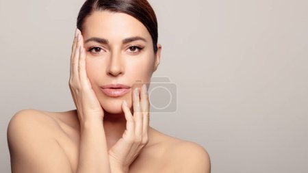 Photo for Confident young woman with glowing, rejuvenated skin and brown hair. She exudes self-assurance and practices self-care. Studio portrait captures her fresh, moisturized face and natural beauty. - Royalty Free Image