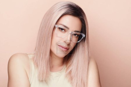 Photo for Young woman with long blonde hair, brown eyes and glasses. Flawless and rejuvenated skin. Trendy hairstyle, stylish glasses. Front view that exudes beauty and style. Represents youth and anti-aging. - Royalty Free Image