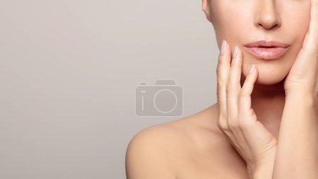 A young woman with radiant, hydrated skin reflects natural beauty and self-care against a gray background. Her calm expression and attractive features show the effects of rejuvenating skin care.