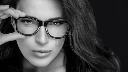 Photo for Close up Gorgeous Woman Holding her Eyeglasses While Looking at Camera. Cool Trendy Eyewear Portrait isolated on Black Background - Royalty Free Image