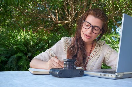 Photo for A young woman with glasses working with her vintage laptopoutdoors, surrounded by nature. - Royalty Free Image