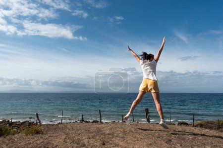 Foto de Mujer segura salta al aire libre en la orilla del océano, capturando un momento real de bienestar y libertad. - Imagen libre de derechos