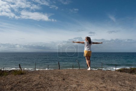 Téléchargez les photos : Une femme confiante au bord d'un océan apaisant, profitant d'un moment d'autosoin. Le ciel et l'horizon de rêve ajoutent à l'atmosphère sereine de cette scène authentique en plein air. - en image libre de droit