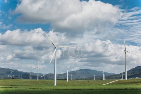 Windmühlen vor blauem Himmel mit Wolken, die erneuerbare Energien und nachhaltige Technologie in einer natürlichen Umgebung darstellen.