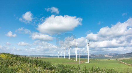 Téléchargez les photos : Un champ serein avec des moulins modernes générant de l'énergie propre sous un vaste ciel bleu parsemé de nuages. - en image libre de droit