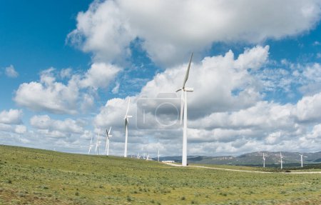 Photo for Sustainable energy concept with windmills against a blue cloudy sky spanning rolling green hills - Royalty Free Image