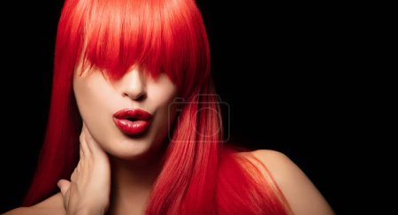 Schönes Model mit leuchtend roten Haaren und frechen Lippen, die vor schwarzem Hintergrund posieren. Das Bild hebt gesunde gefärbte Haare und eine moderne Frisur hervor. Horizontales Format.