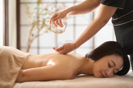 Téléchargez les photos : Esthéticienne goutte à goutte huile de massage au salon de beauté - en image libre de droit