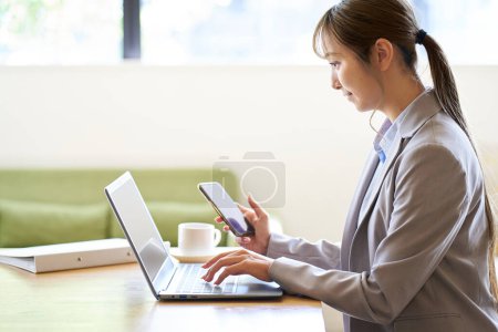 Photo for Asian woman operating a computer and smartphone at a cafe - Royalty Free Image