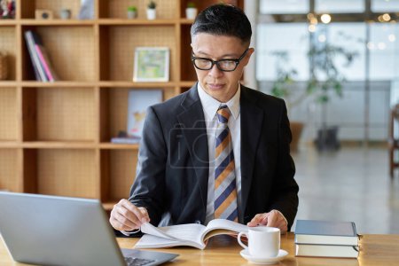 Téléchargez les photos : Asiatique homme d'affaires lecture dans un café pour étudier - en image libre de droit