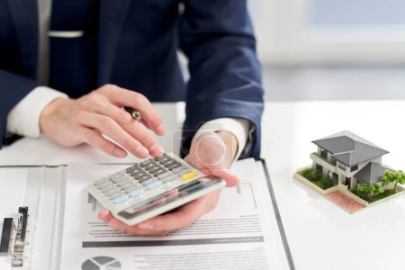 Téléchargez les photos : Homme d'affaires calculant de l'argent lié à l'immobilier - en image libre de droit
