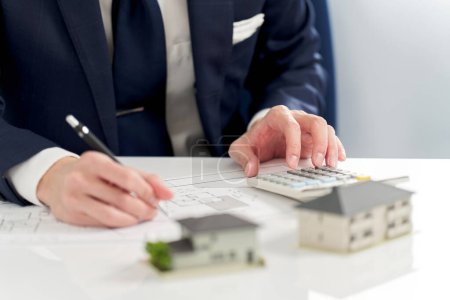 Téléchargez les photos : Homme d'affaires calculant le plan d'étage de l'immobilier - en image libre de droit