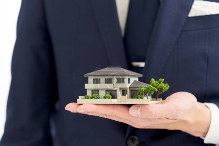 Hand eines Geschäftsmannes mit einem Modell eines Hauses