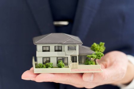 Hand eines Geschäftsmannes mit einem Modell eines Hauses