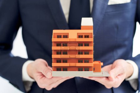 Die Hand eines Geschäftsmannes hält ein Modell einer Wohnung