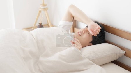 Ein Mann misst im Schlaf seine Temperatur mit einem Thermometer