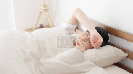 Foto de Un hombre mide su temperatura con un termómetro mientras duerme - Imagen libre de derechos