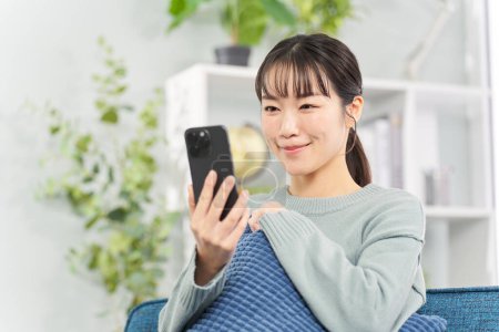 Femme assise sur le canapé et regardant smartphone
