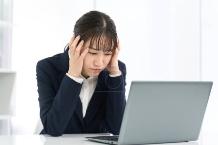 Mujer de negocios sosteniendo la cabeza frente a una computadora