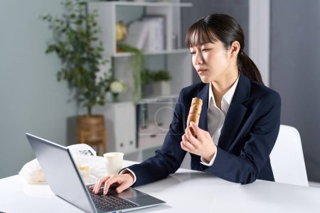 Téléchargez les photos : Femme d'affaires travaillant tout en mangeant une collation tard dans la nuit - en image libre de droit