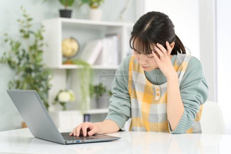 A woman wearing an apron holding her head while working on a computer