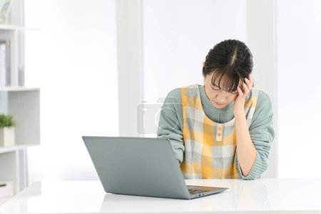 A woman wearing an apron holding her head while working on a computer