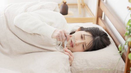 Foto de Una mujer midiendo su temperatura con un termómetro mientras duerme - Imagen libre de derechos