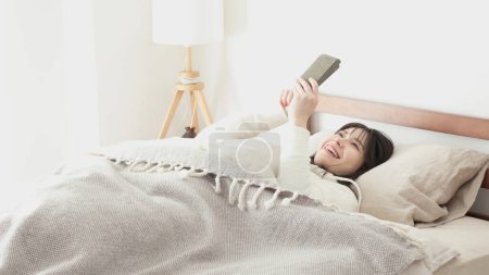 Mujer asiática mirando el teléfono inteligente después de despertar