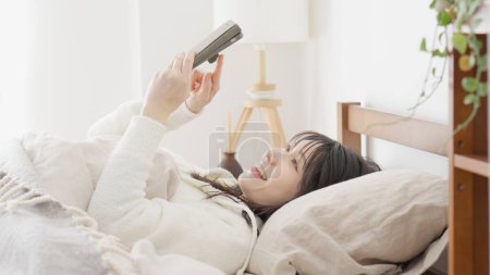 Asian woman looking at smartphone after waking up