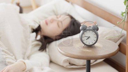 Eine Frau, die ihren Wecker ausschaltet und wieder einschläft