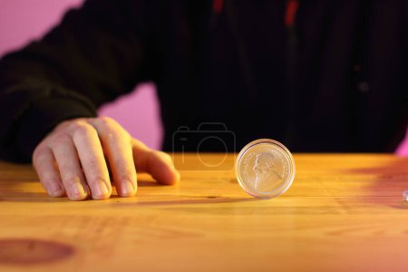 Téléchargez les photos : Un krugerrand argenté sur une table avec une lumière jaune et la main d'une personne en arrière-plan - en image libre de droit
