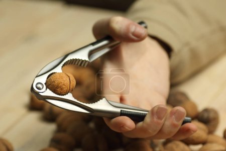 Téléchargez les photos : Nutcracker in hand with a walnut on the background of the table - en image libre de droit