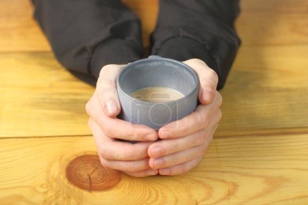 Foto de A person holds a cup with coffee in both hands on a wooden table - Imagen libre de derechos