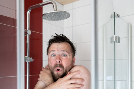 Foto de El hombre europeo toma una ducha bajo agua fría, se congela y se ve miserable. Concepto de ahorro y crisis energética. - Imagen libre de derechos