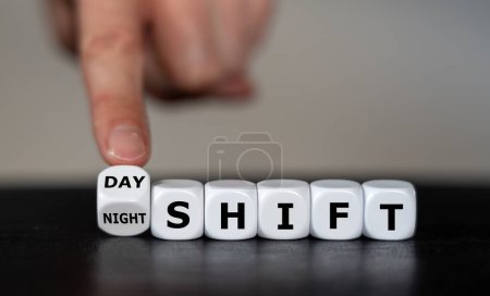 Photo for Hand turns dice and changes the  expression 'day shift' to 'night shift'. - Royalty Free Image
