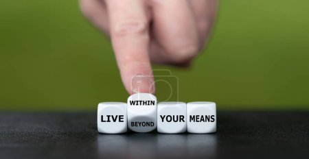 Foto de La mano gira los dados y cambia la expresión 'vivir más allá de tus medios' a 'vivir dentro de tus medios'. - Imagen libre de derechos
