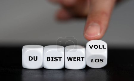 Téléchargez les photos : Main tourne les dés et change l'expression allemande "du bist wertlos" (vous ne valez rien) en "du bist wertvoll" (vous êtes précieux). - en image libre de droit