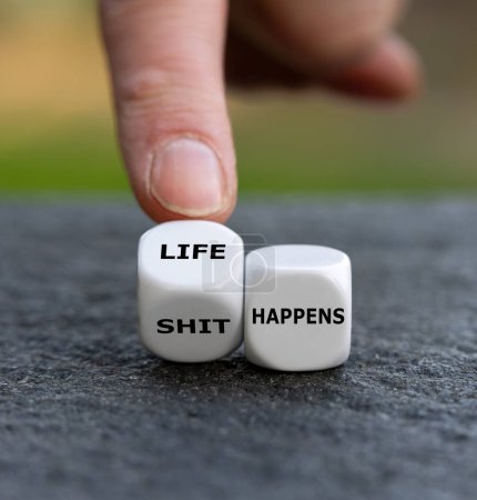 Hand turns dice and changes the expression 'shit happens' to 'life happens'.