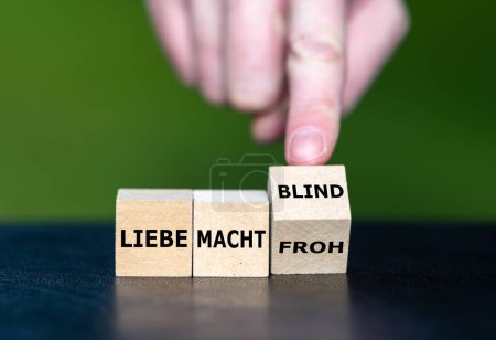 Photo for Hand turns wooden cubes and changes the German saying 'liebe macht froh' (love makes happy) to 'liebe macht blind' (love makes blind). - Royalty Free Image