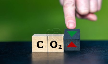 Symbol for reducing CO2 emissions. Hand turns a wooden cube and changes the orientation of an arrow from up to down.