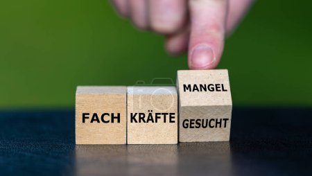 Hand dreht Holzwürfel und wandelt den deutschen Ausdruck "Fachkraefte gesucht" in "Fachkraeftemangel" um).