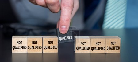 Foto de Symbol for finding a qualified candidate. Hand picks wooden cube with the text 'qualified' instead of cubes with the text 'not qualified'. - Imagen libre de derechos