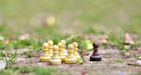 Photo for Symbol for excluding someone who is different. A group of white chess figueres is seperated from a single black figure. - Royalty Free Image