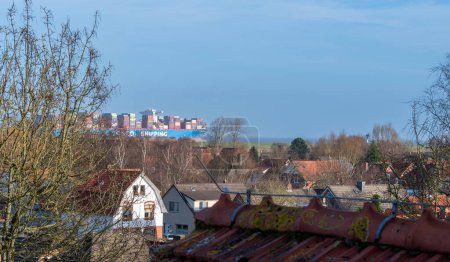 Foto de Huge container ship on the river Elbe passing the village Altenbruch near Cuxhaven, Germany at the 25th of December 2023. - Imagen libre de derechos