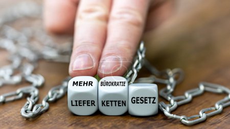 Hand turns dice and changes the German expression 'Lieferkettengesetz' (Supply chain act) to 'mehr buerokratie Gesetz' (more bureaucracy law).