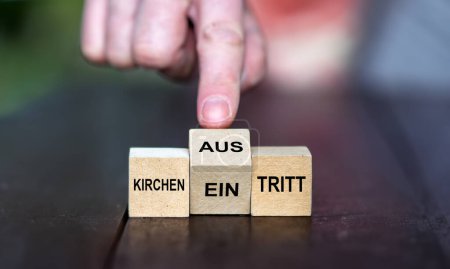 Hand turns wooden cube and changes the German expression 'Kircheneintritt' (join the church) to 'Kirchenaustritt' (leave the church).