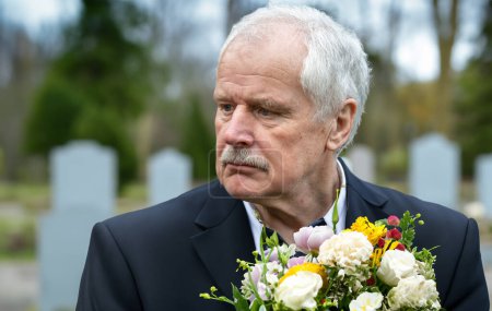 Photo for Sad old man with flowers mourning at the graveyard. - Royalty Free Image