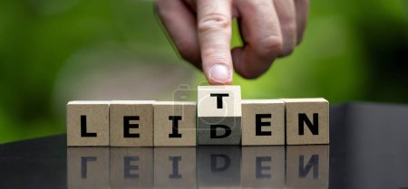 Hand turns wooden cube and changes the German word 'leiden' (suffer) to 'leiten' (lead).